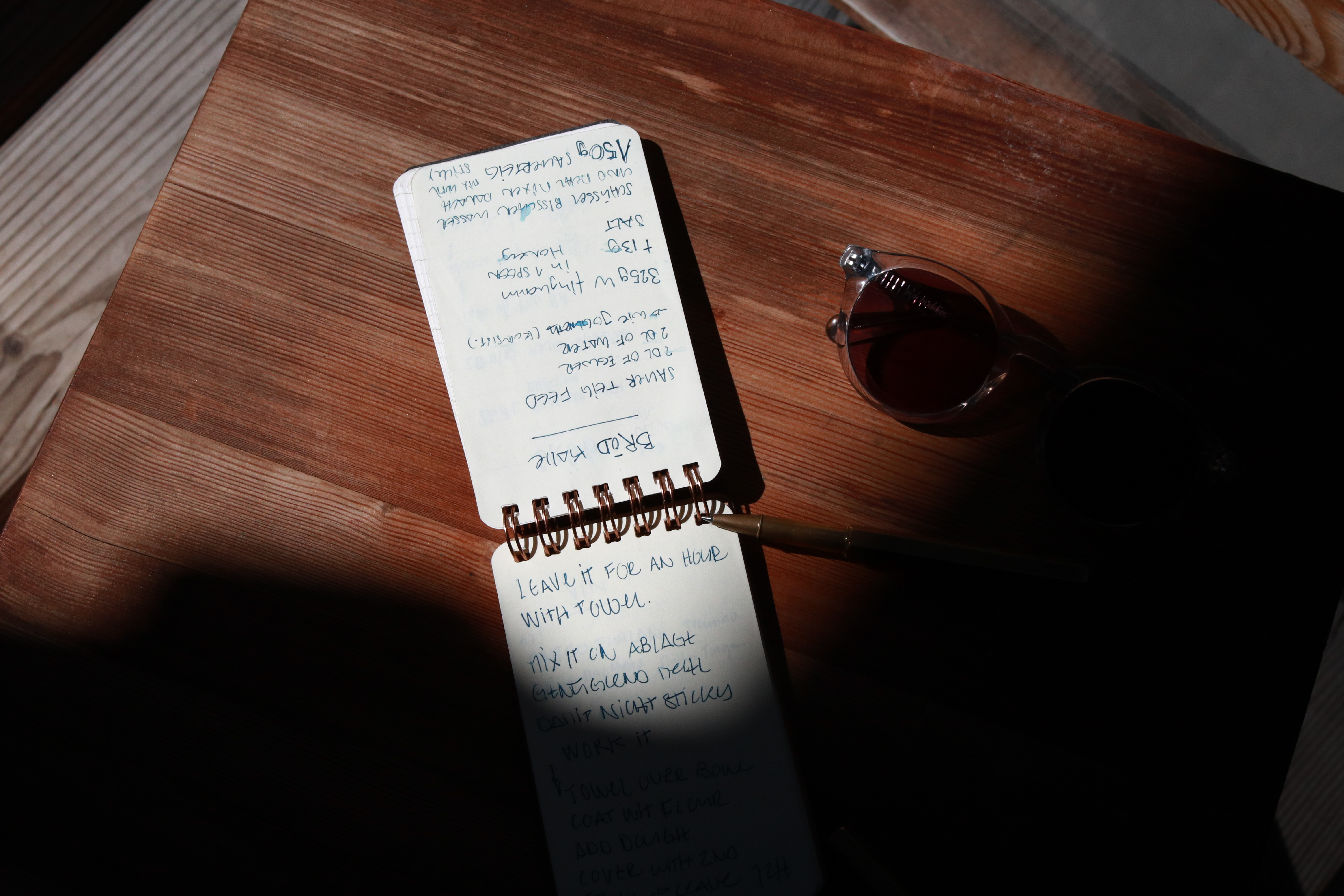 Kleiner Notizblock mit Stift neben einer Sonnenbrille